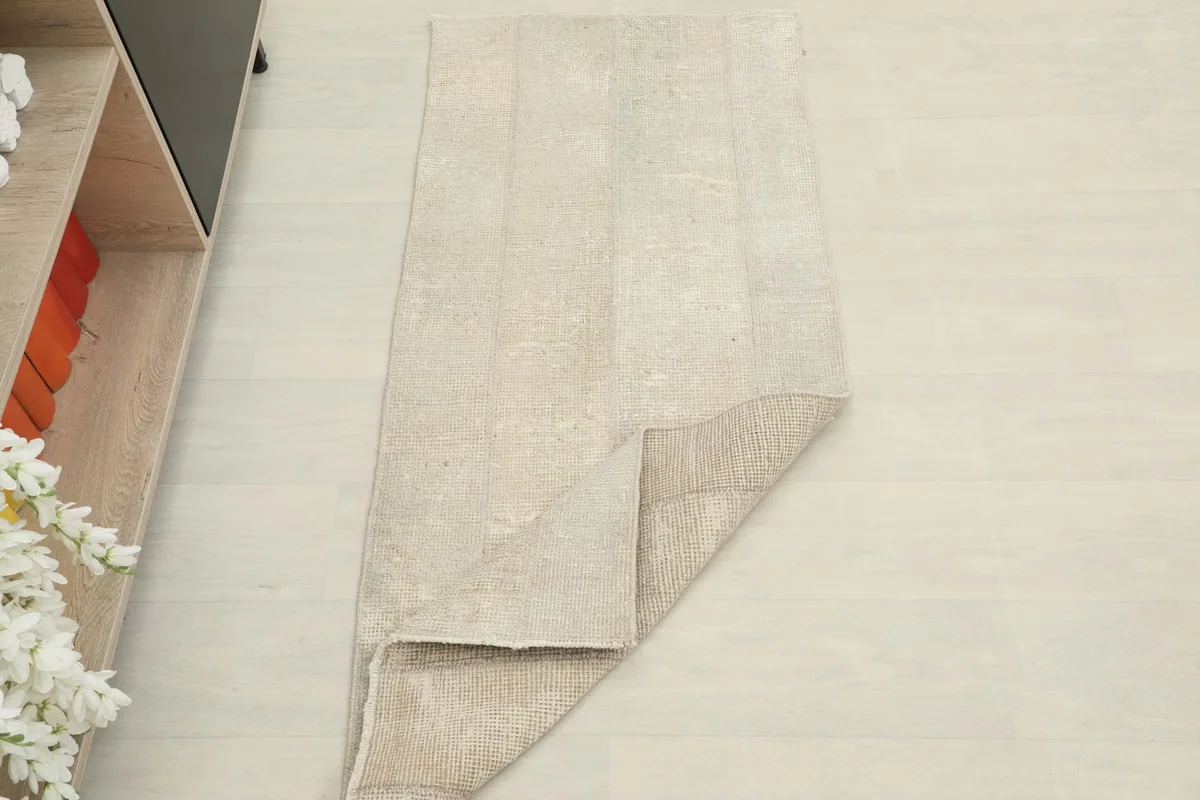 The vintage beige rug partially folded, illustrating its flexibility and construction.