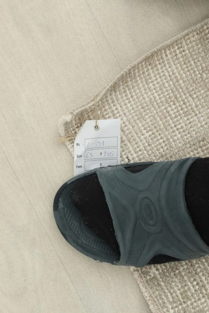 A close-up of the rug's texture next to a sandal for scale, with the size tag visible.