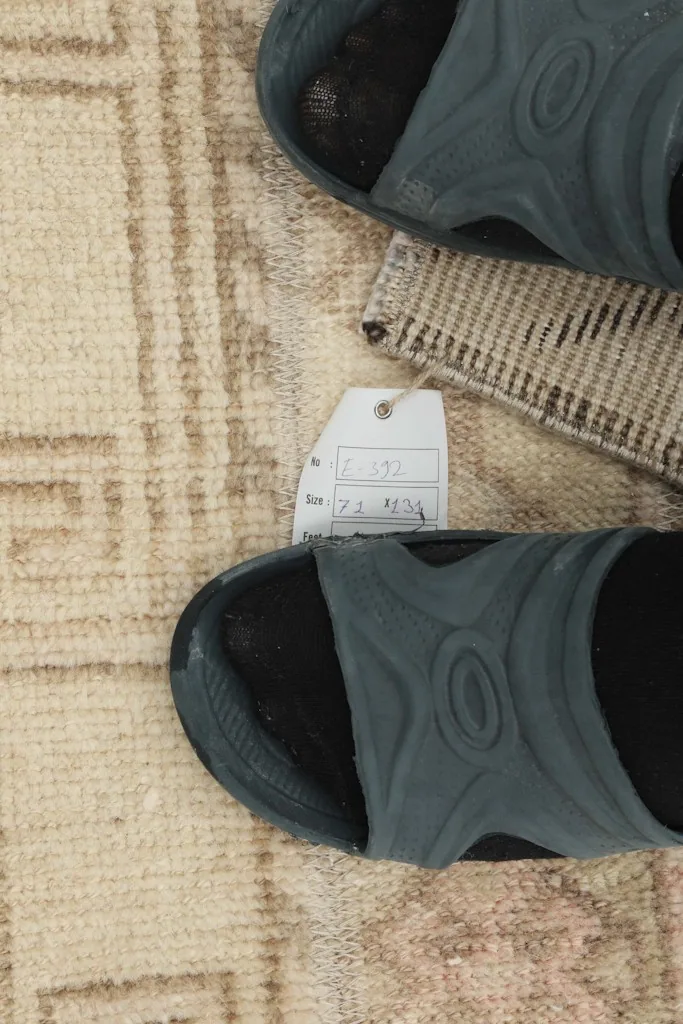 Close-up of the rug with a size tag and sandals for scale, showing texture and color