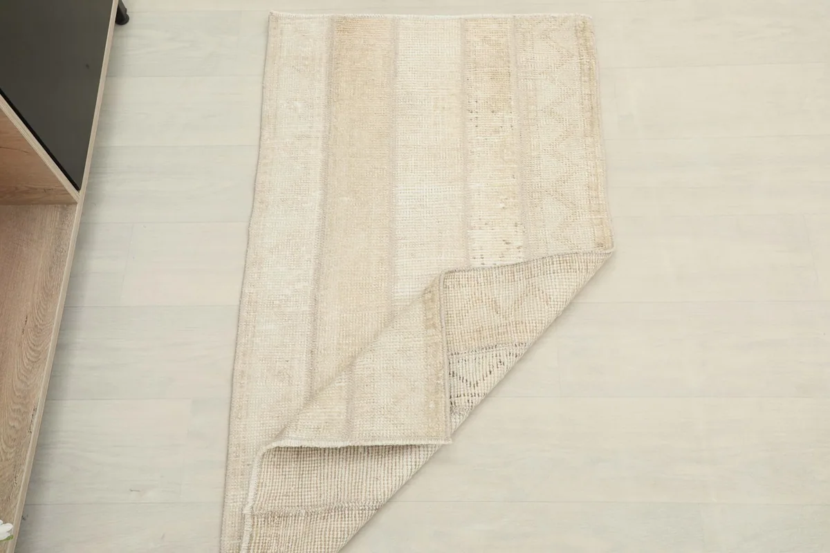 Rug partially folded, placed on a light floor next to shelving, suggesting scale in a home setting.