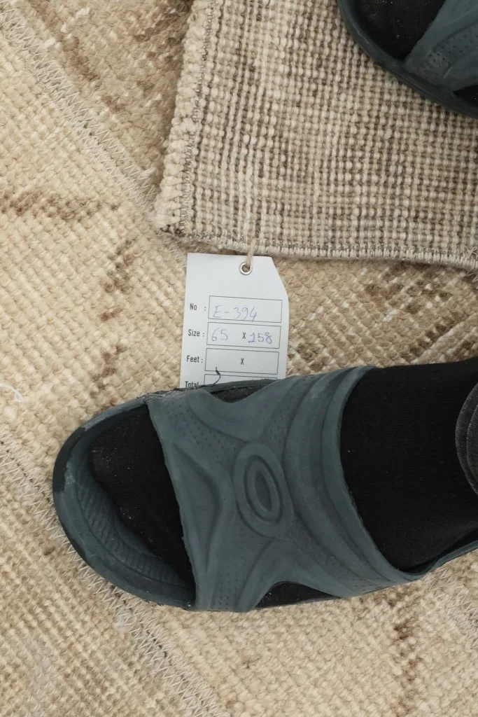 Detail showing the rug's texture next to a foot for scale, with a size tag visible