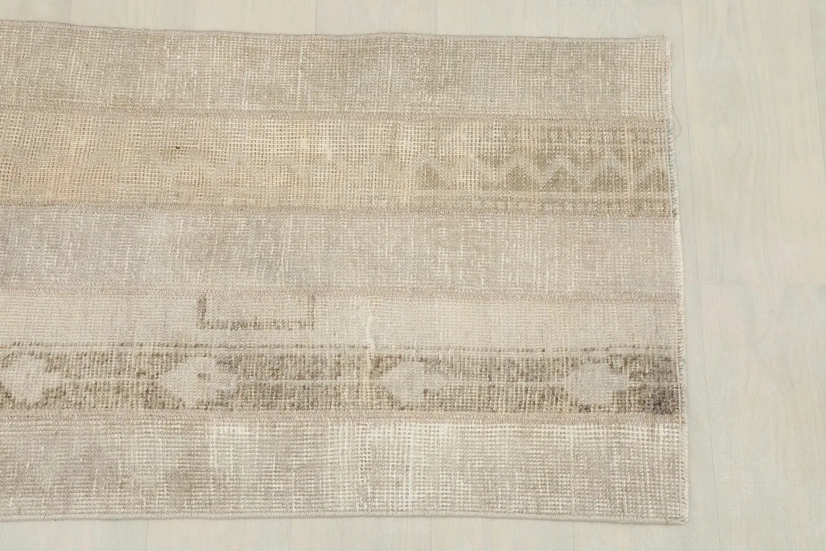 Close-up of the rug's surface, showing faded tan and brown geometric patterns and texture
