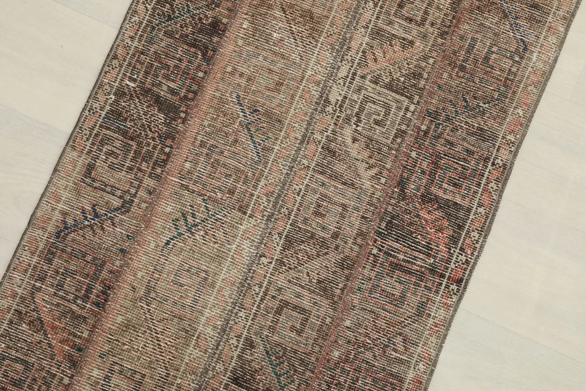 Close-up detail of the rug's surface, showing intricate geometric motifs in brown, tan, rust, and blue.