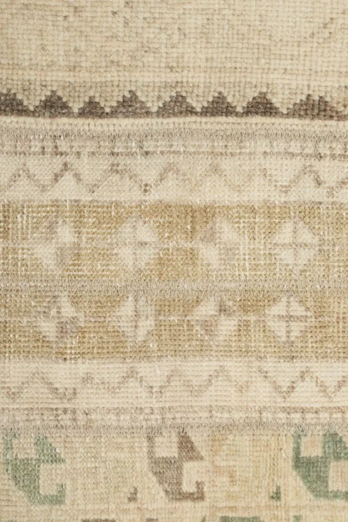 Macro shot of the low wool pile, showing the hand-knotted texture and beige, tan, and olive threads.