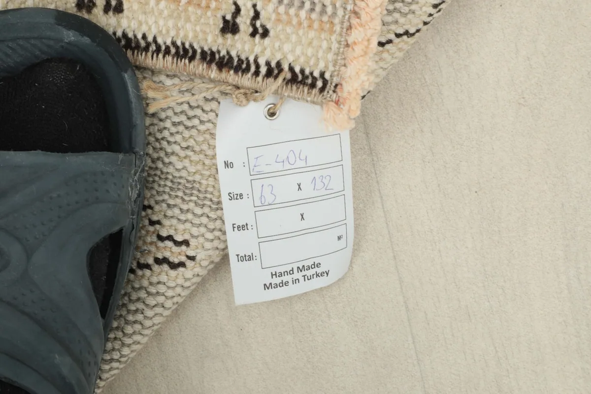 Size tag for the 63 x 132 cm hand-knotted rug from Turkey next to a shoe for scale