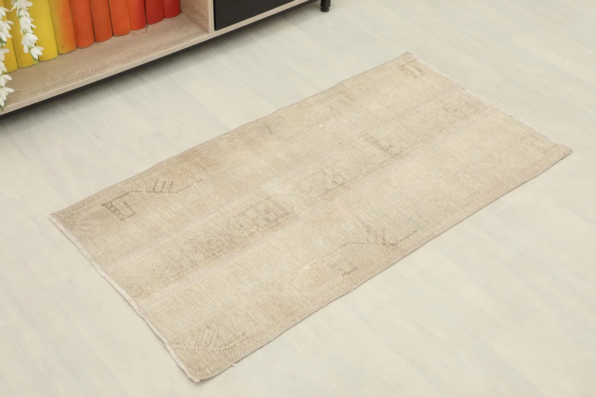 Angled view of the tan vintage rug, showing its rectangular shape and faded geometric motifs
