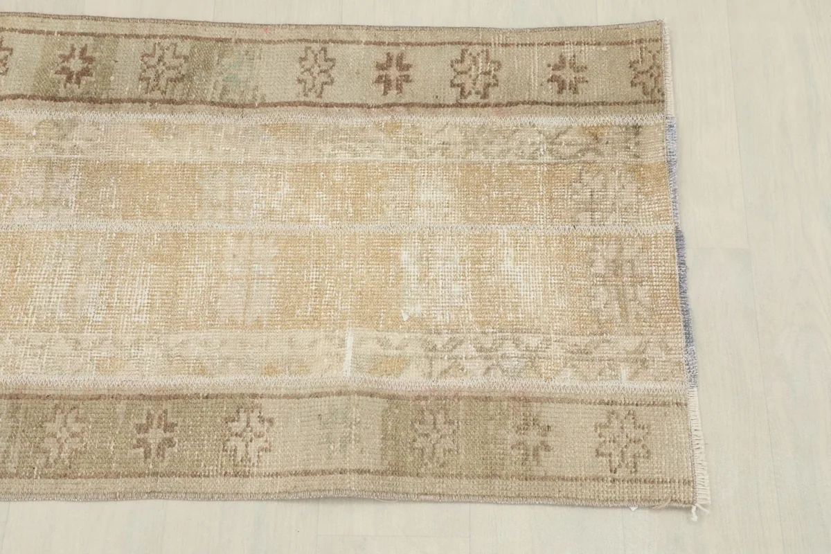 Close-up view of one end of the rug, showing the faded beige field and tribal border motifs.
