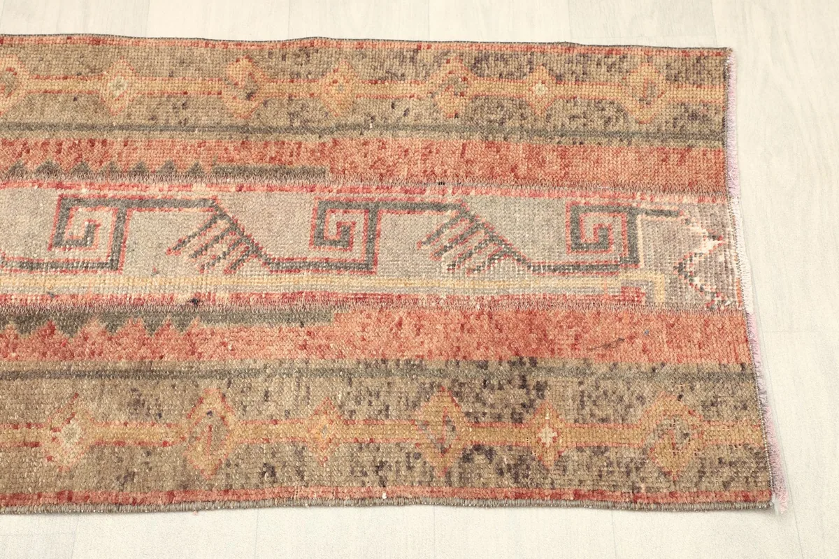 Angled view of one end of the rug, showing the blend of rust, beige, and gray stripes and patterns.