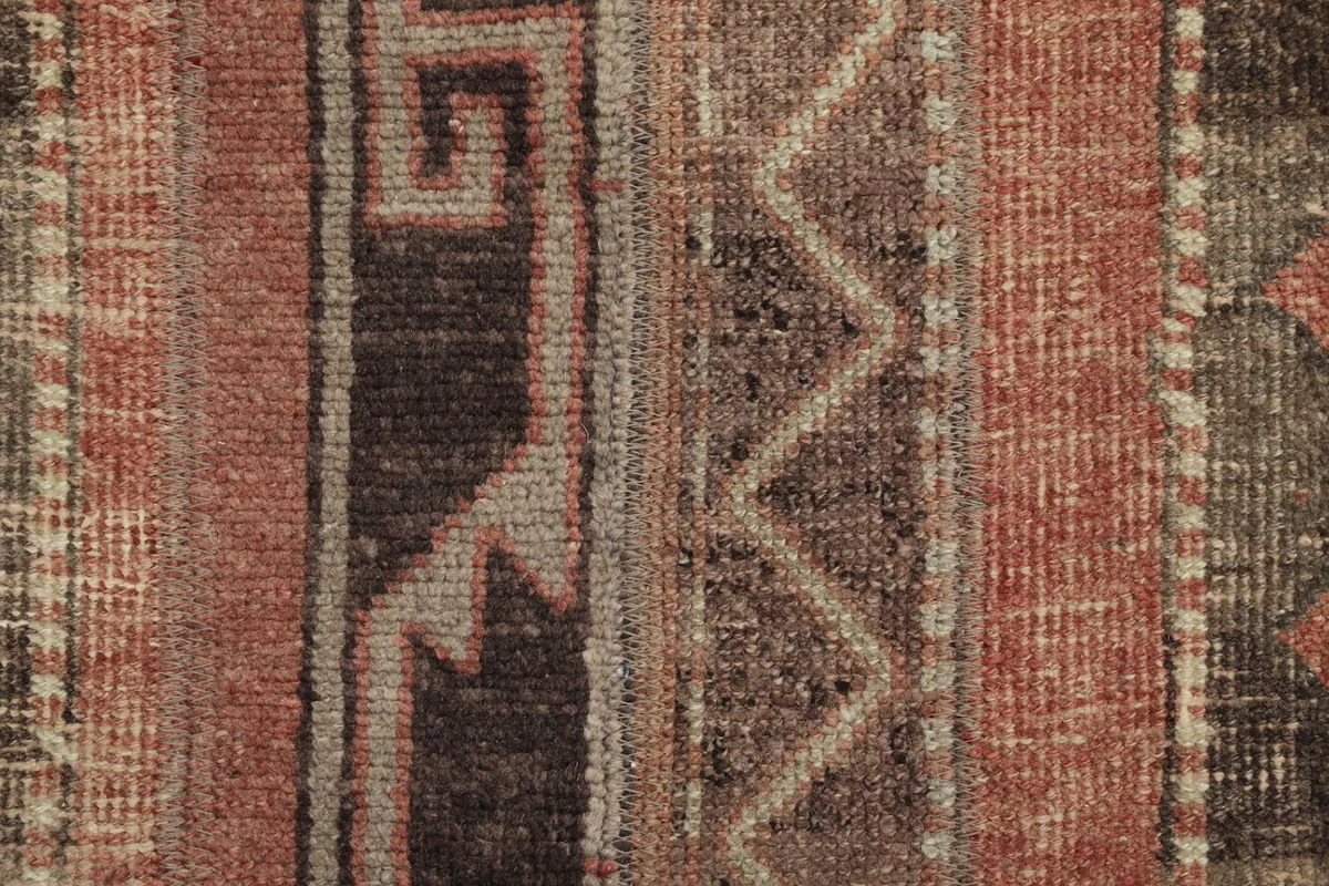 Close-up detail of the hand-knotted wool pile and geometric patterns in rust and brown.