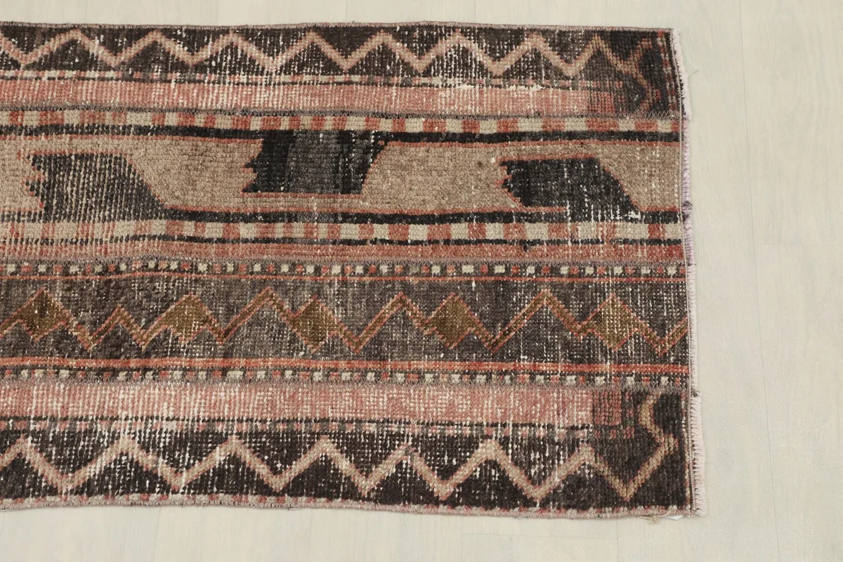 Close-up of one end of the rug, detailing the zigzag and striped patterns in brown, beige, and rose