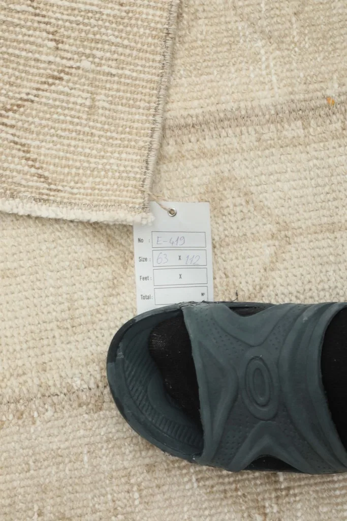Close-up of the rug's texture with a size tag and a sandal for scale.