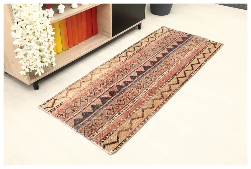 Full top view of the 2'1" x 5'2" rust and tan tribal runner on a light floor, next to a bookshelf
