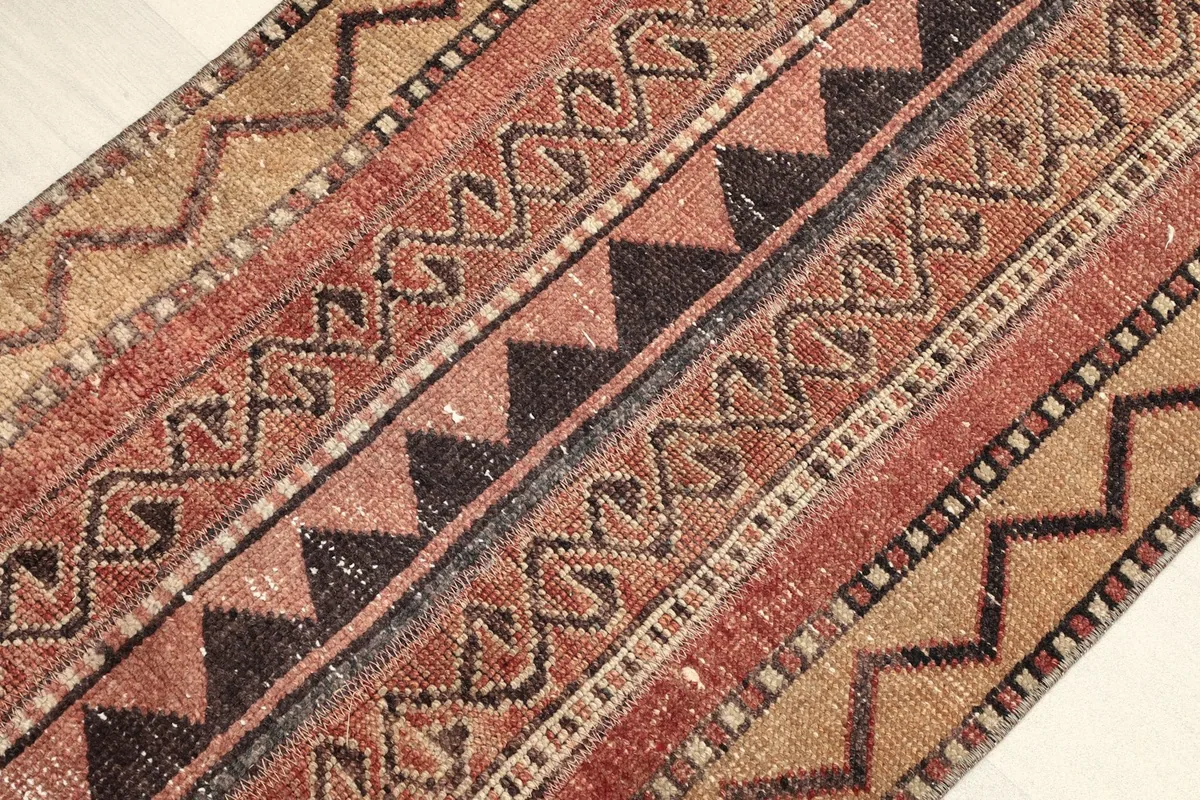 Angled close-up of the rug's surface, showing various geometric and tribal patterns in rust, tan, and black