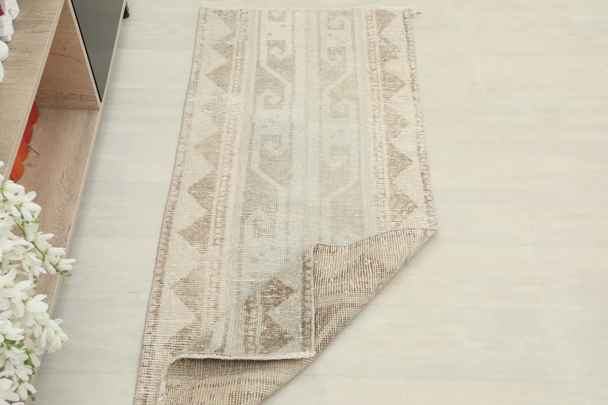 The beige and tan rug partially folded, placed in a room to show its scale and color.