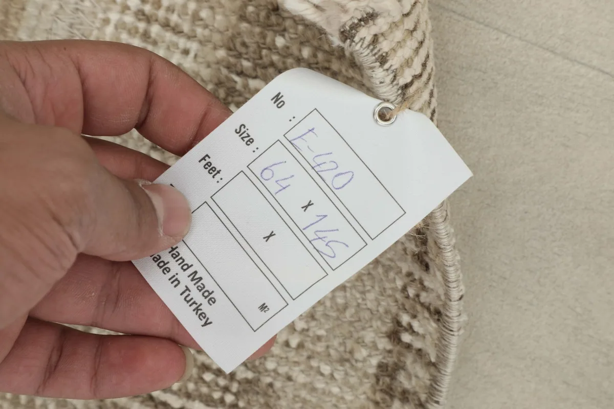Hand holding a tag showing the rug's dimensions in centimeters and confirming handmade origin.