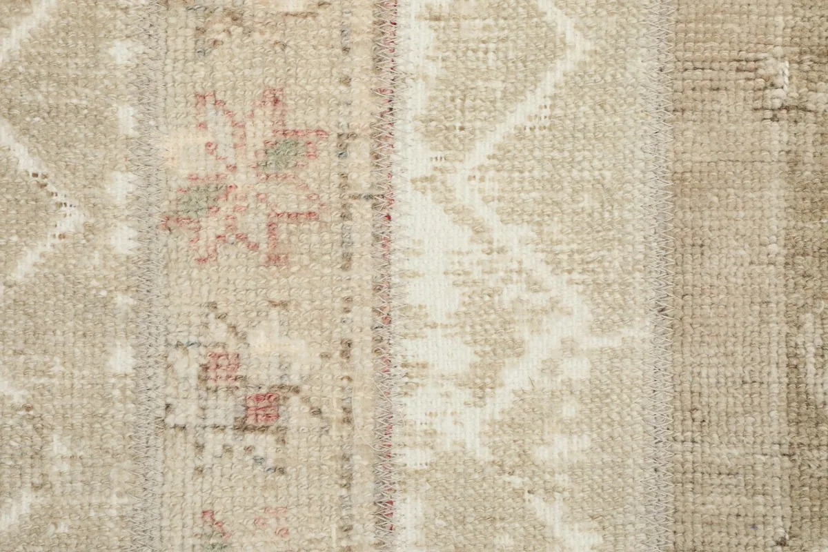 Macro detail of the hand-knotted wool pile showing a faded pink floral-like motif