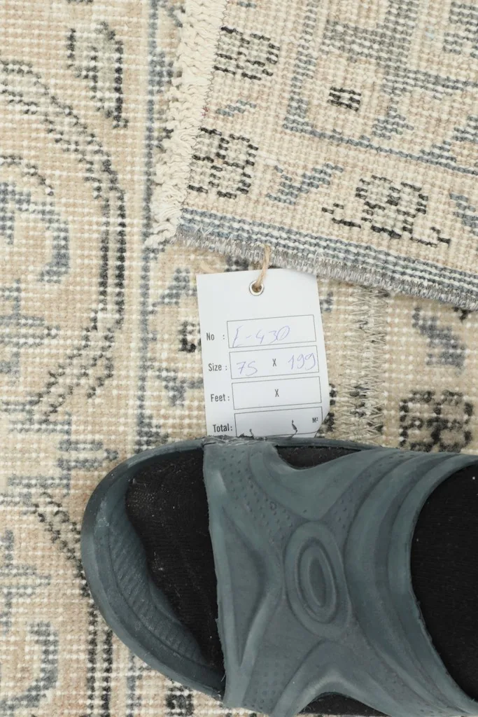 Close-up of a size tag and a sandal on the rug, providing a scale reference for the rug's texture and pattern.