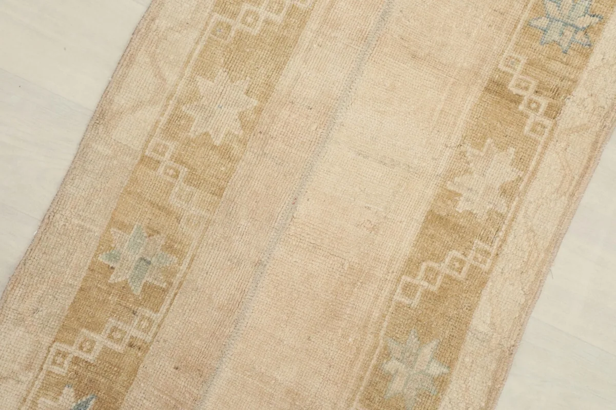 Close-up detail of the rug's geometric star motifs and border patterns in beige, tan, and blue.