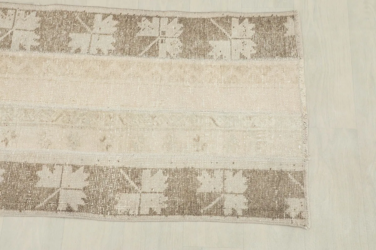 Close-up view of the tan geometric panel with leaf-like motifs on the vintage rug.