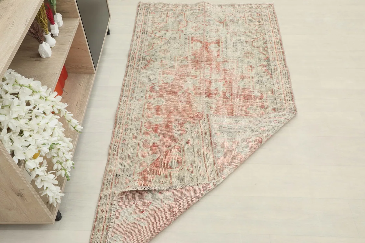 Rug partially folded, displaying the back and front texture, with faded rose and beige patterns visible.