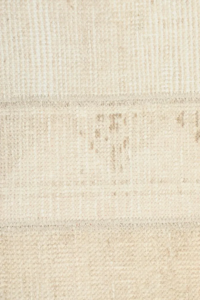 Detailed view of the rug's low pile and some areas of natural wear and patina within a beige patch