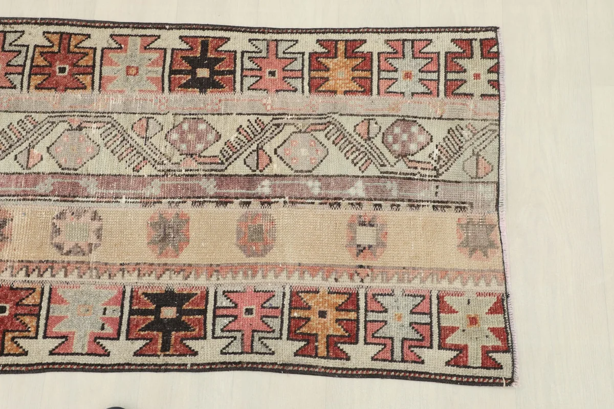Close-up view of the rug's beige field and geometric designs in rust, pink, and black