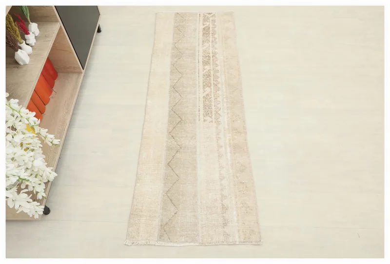Full overhead view of the beige and brown tribal geometric vintage runner rug on a white floor.