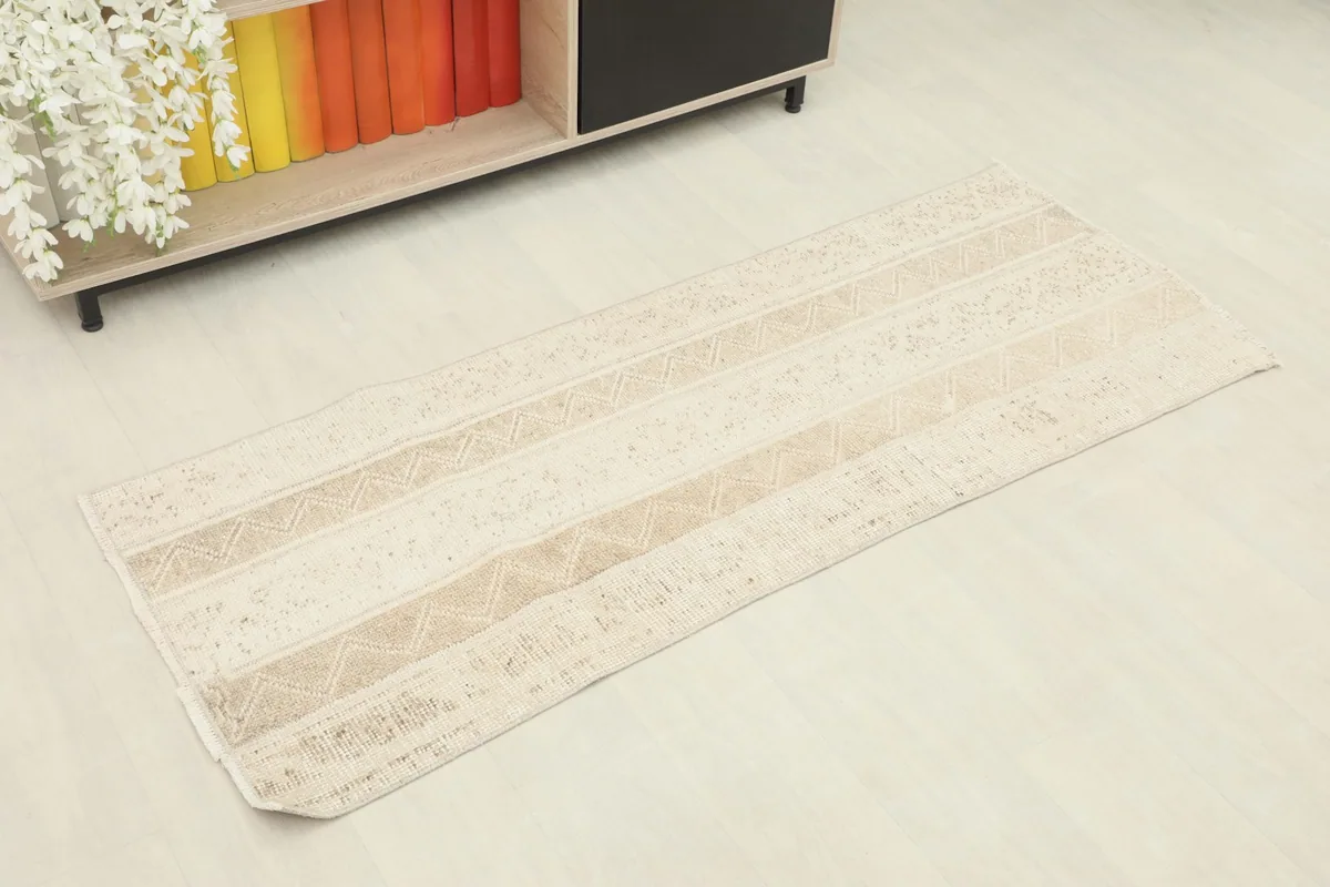 Angled view of the beige and tan runner rug placed on a light floor, next to a cabinet.