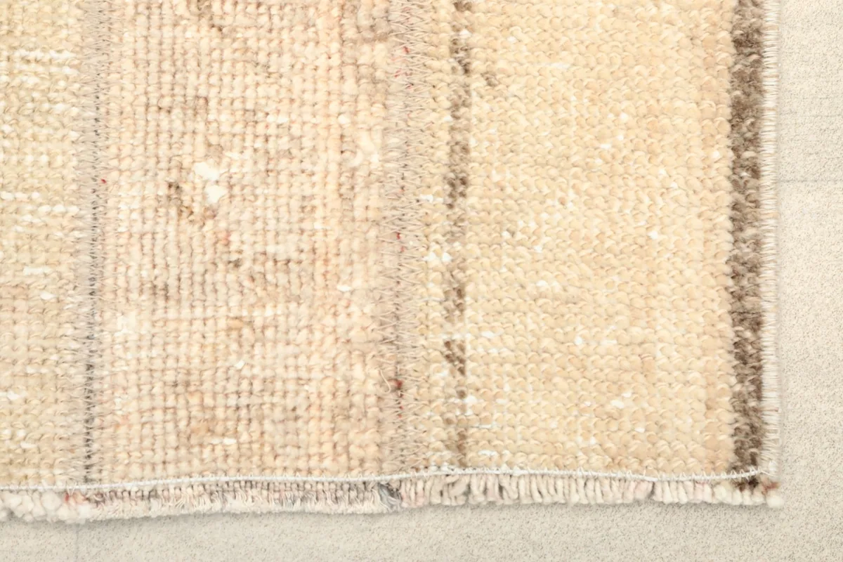 Close-up view showing the low wool pile and textured surface of the beige and tan rug.