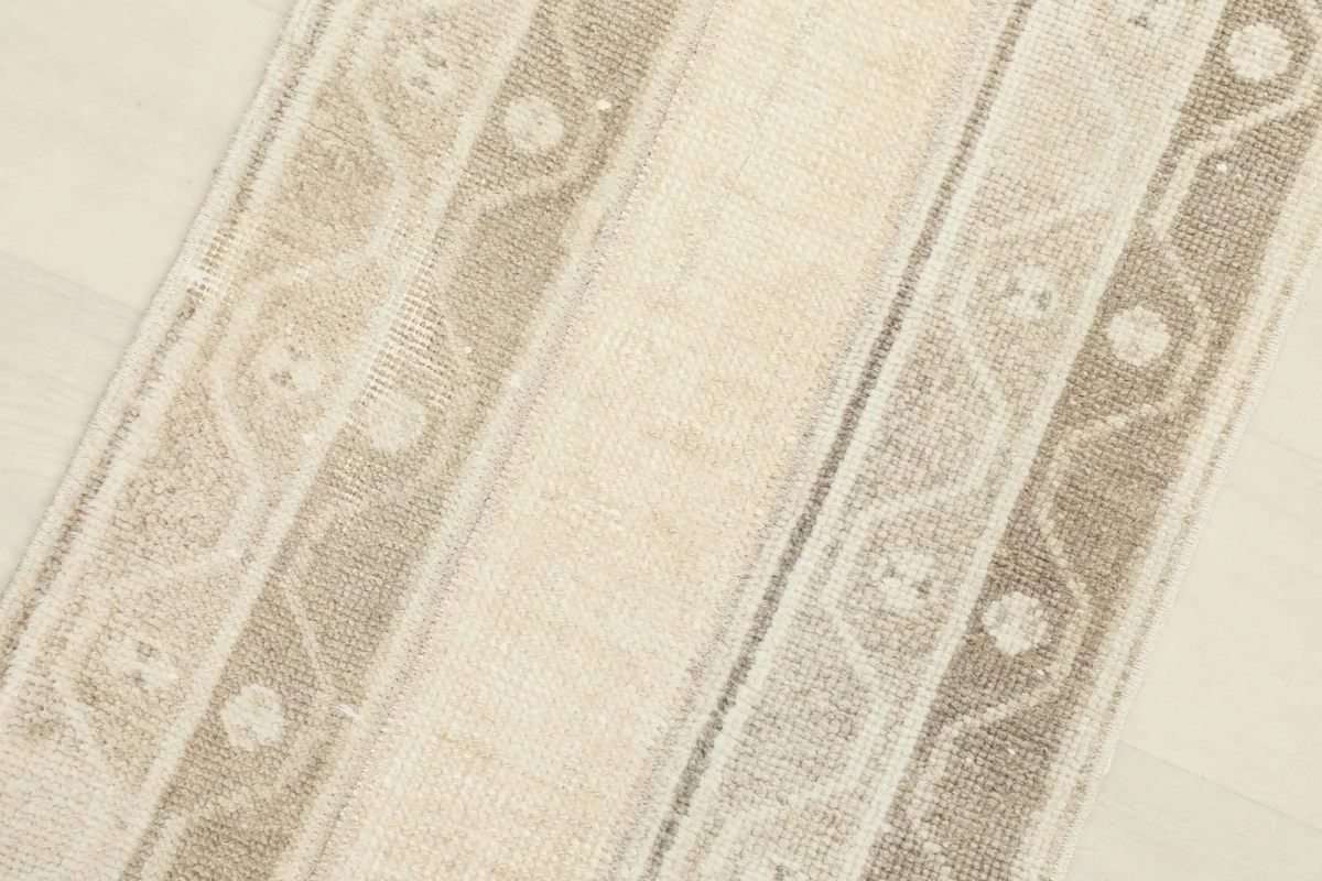 Detailed view of the central beige field and adjacent tan patterned bands of the vintage wool rug.