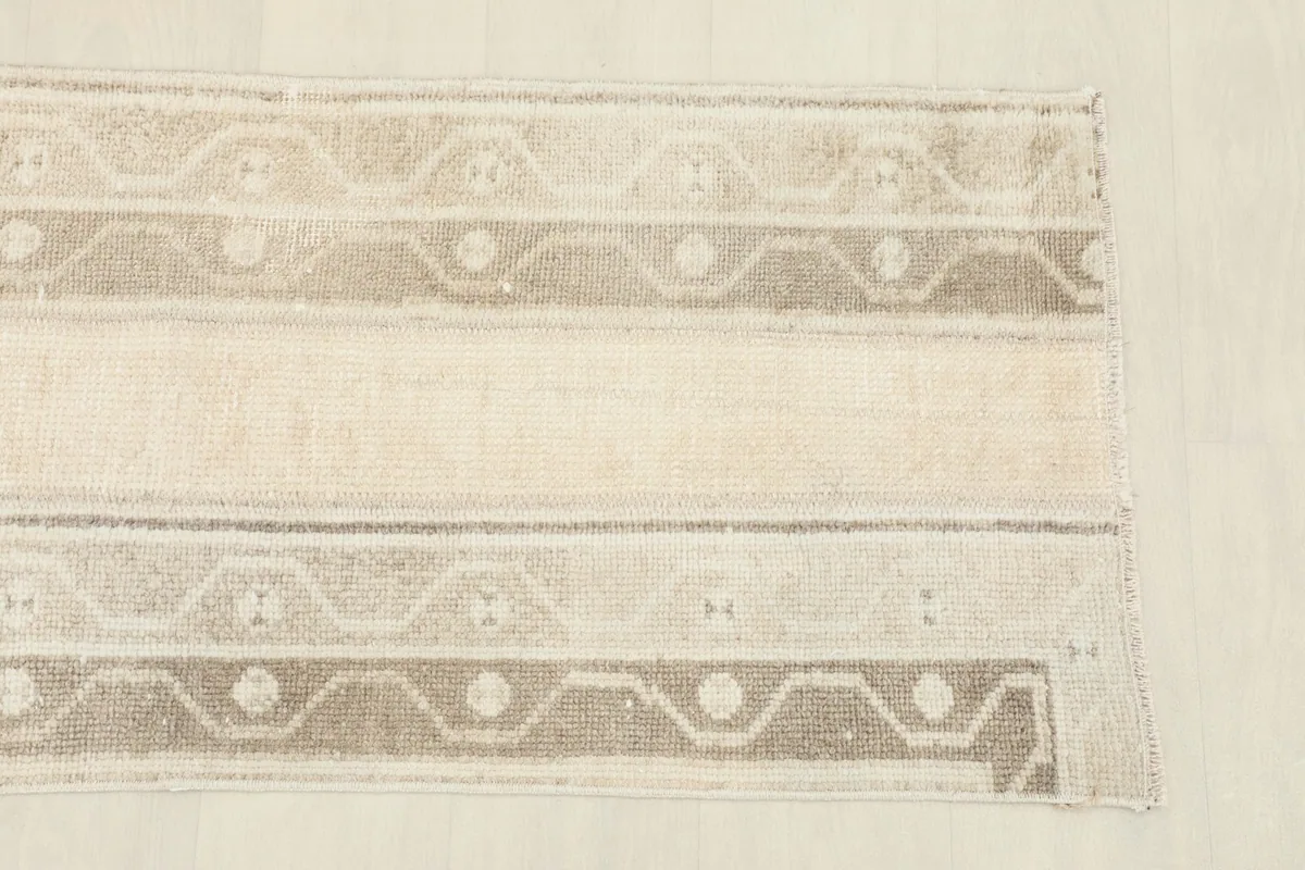 Overhead view focusing on the upper portion of the beige and tan rug, showing pattern detail and color variations.