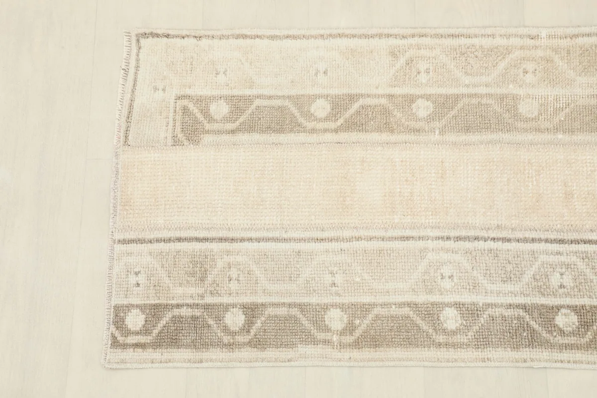 Close overhead view of one end of the rug, detailing the beige and tan geometric patterns and border.