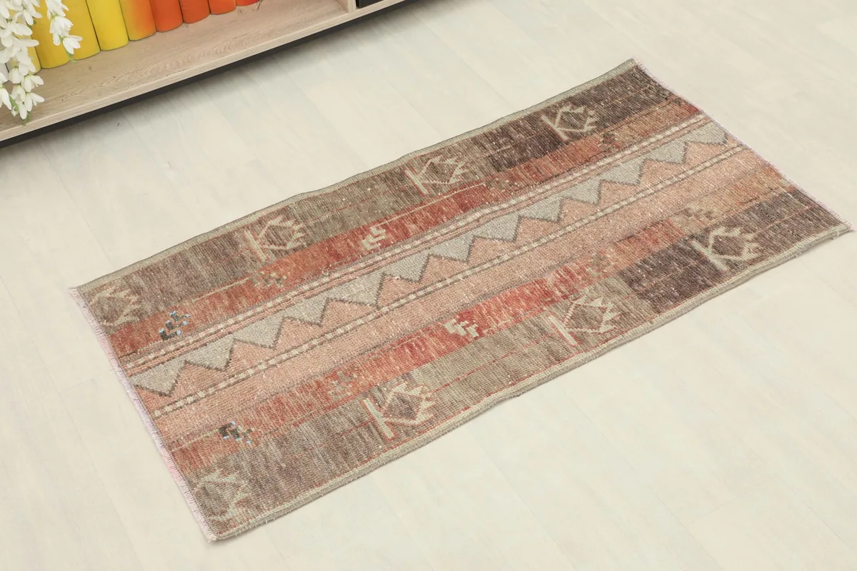 Angled view of the mini rug showcasing its geometric and tribal patterns in rust, rose, and gray tones.