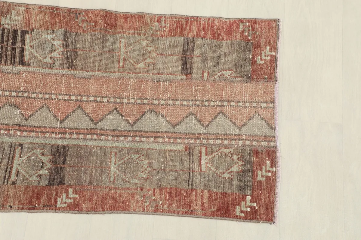 Close-up of one end of the rose and brown rug, showing the tribal motifs and distressed texture.