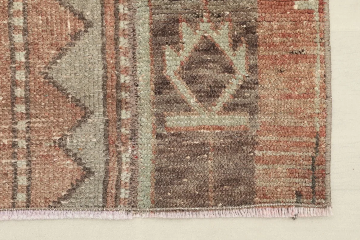 Close-up of the short, textured fringe and the edge of the rose and brown hand-knotted rug.