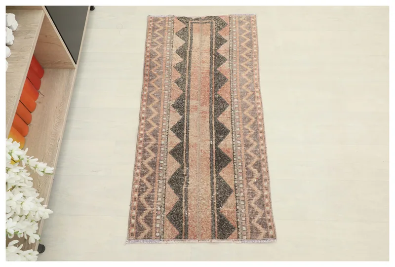 Full overhead view of the rose and charcoal geometric vintage Anatolian rug on a white floor.