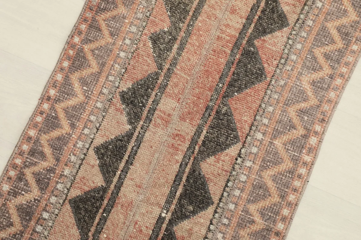 Close-up of the central charcoal geometric motifs and the surrounding rose and beige field.