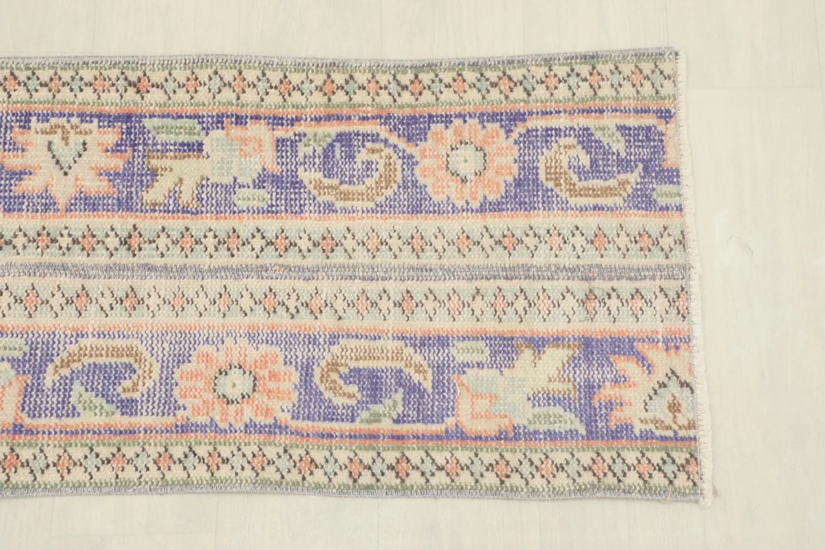 Close-up of one end of the runner rug, showing purple, beige, and rose floral and geometric motifs.