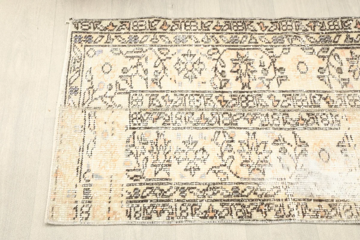 Angled top view of the rug's left side, showing the border and field patterns with a gentle patina.