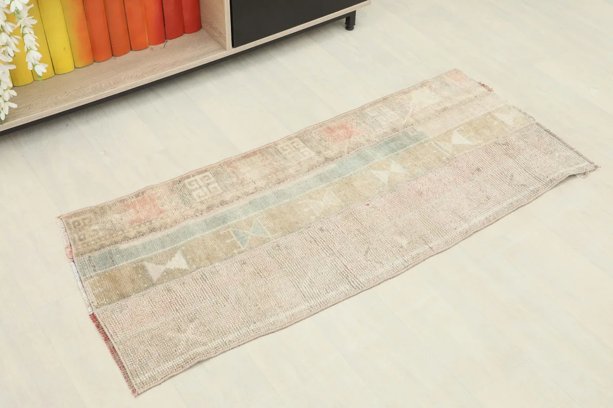Angled view of the vintage Anatolian rug showcasing its beige, rose, and blue geometric patterns in a room setting.