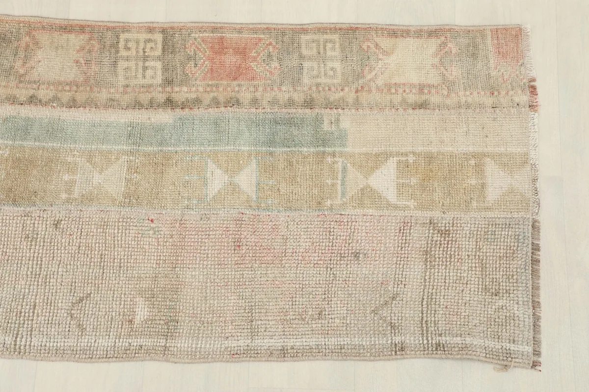Close-up detail of the rug's surface, showing the distinct bands of geometric patterns in beige, rose, and blue tones.
