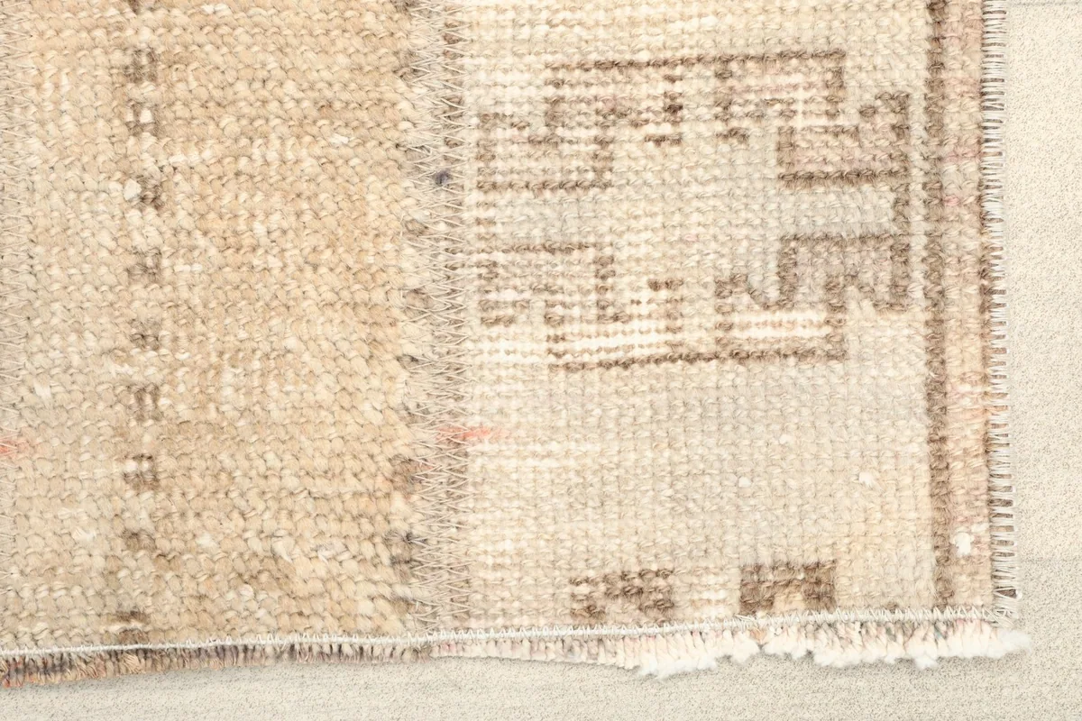 Close-up detail of the rug's patchwork seam and brown tribal motifs on a beige field