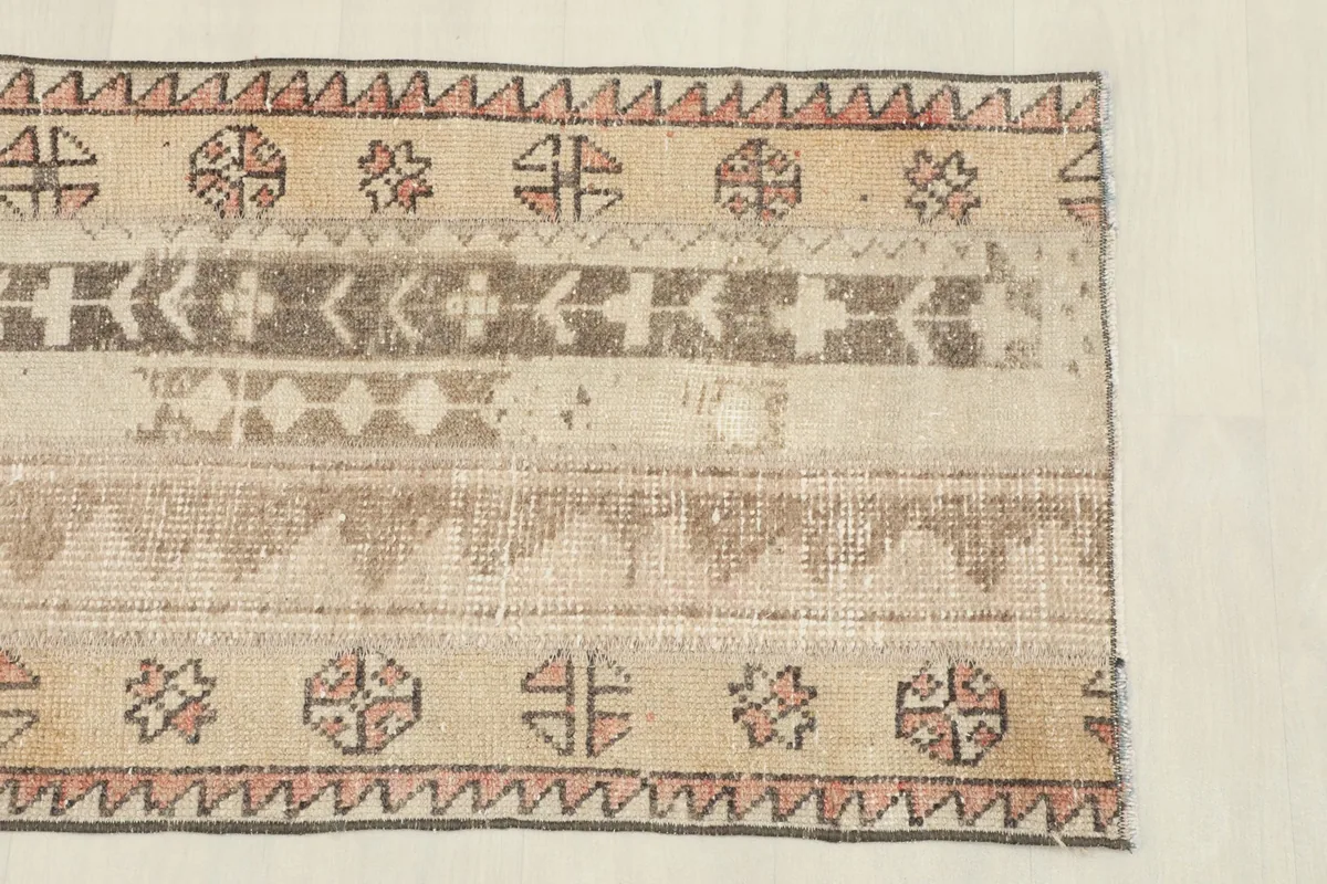 Close-up detail of the rug's patterns, showing beige, brown, and rose tribal motifs and texture.