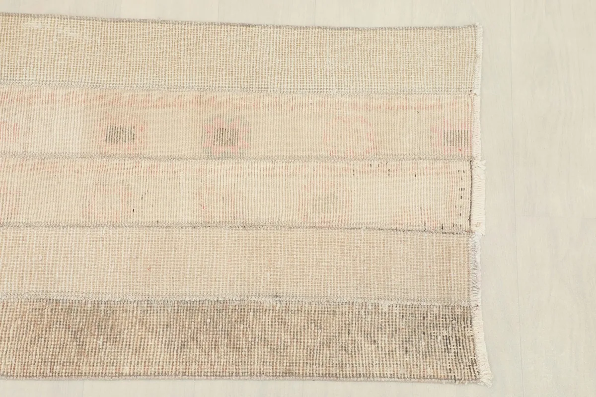 Close overhead view of the rug's surface, highlighting the striped patchwork and subtle rose tones.