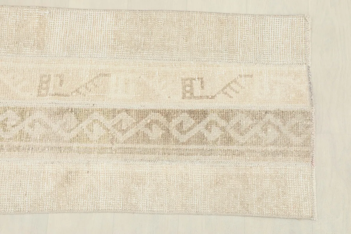 Close-up of one end of the rug, highlighting the beige, cream, and tan geometric tribal motifs.
