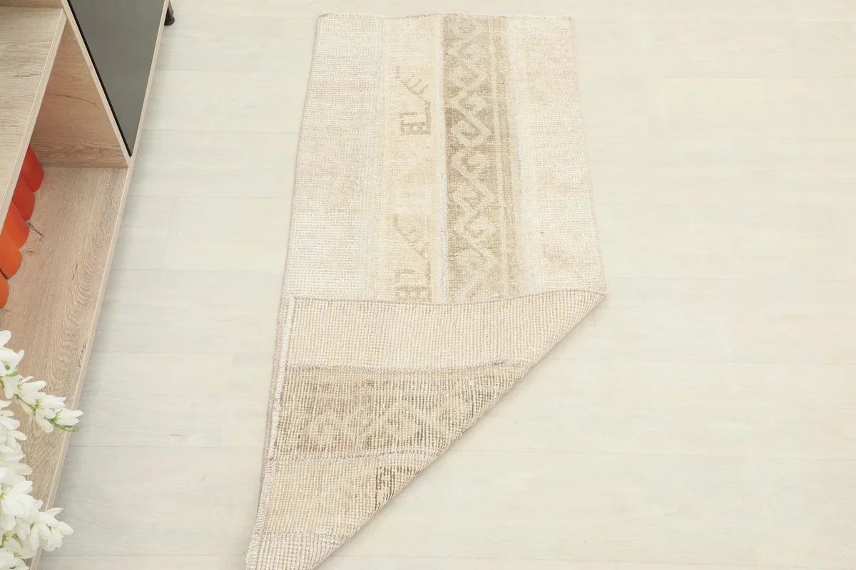 The beige area rug folded at a corner, displaying both the pile and the cotton foundation.