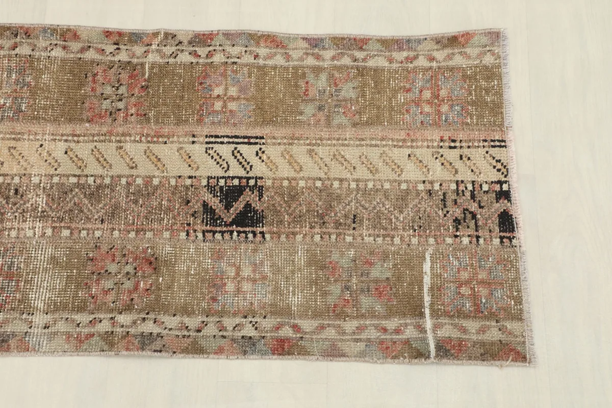 Close-up view of one end of the rug, showing the blend of beige, rose, and black geometric patterns.