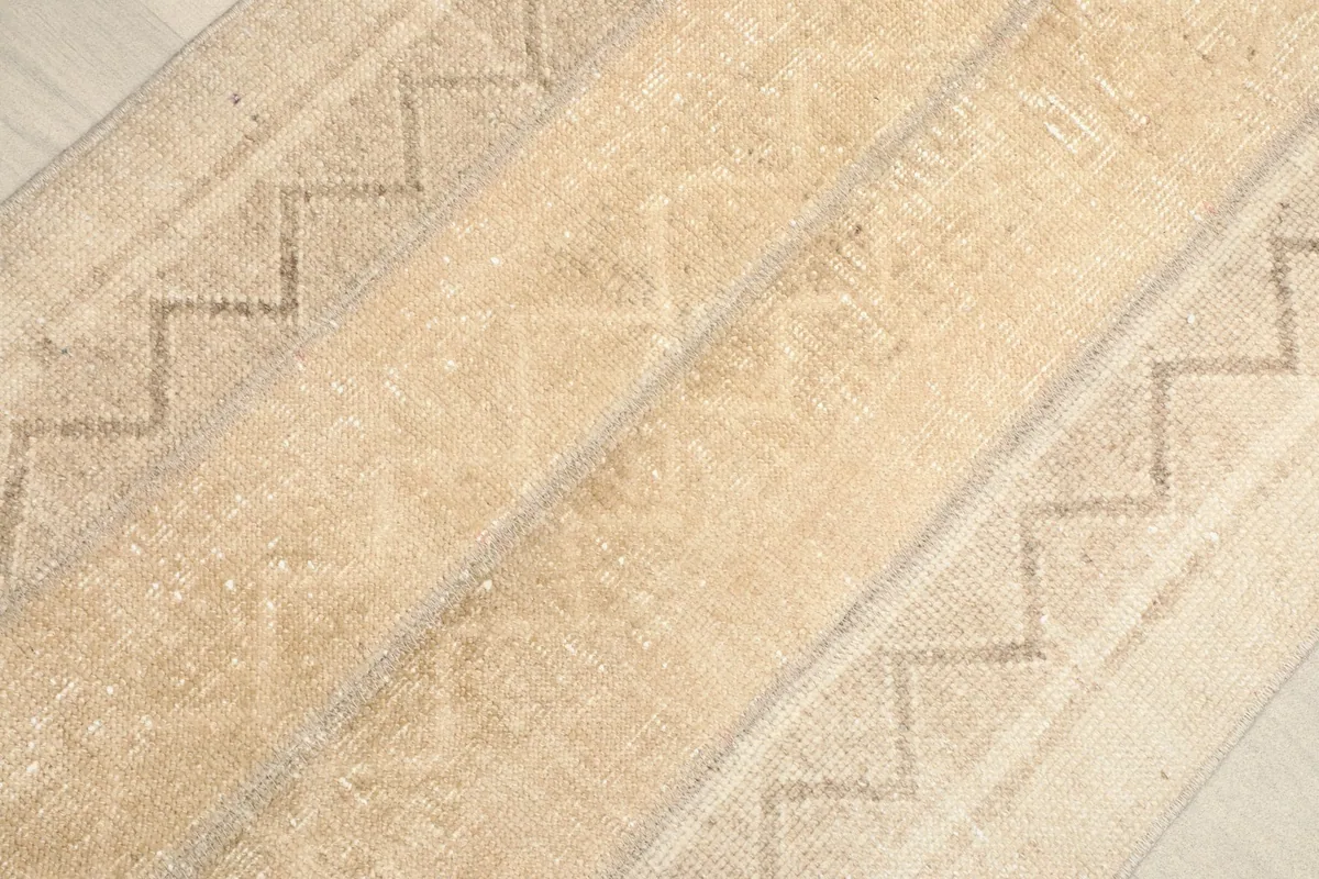 Angled close-up of the beige rug's surface, highlighting the geometric stripe motifs