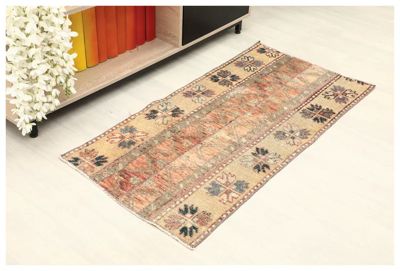 Top view of the 2x4 beige and rust vintage Anatolian rug on a white floor next to a bookshelf.
