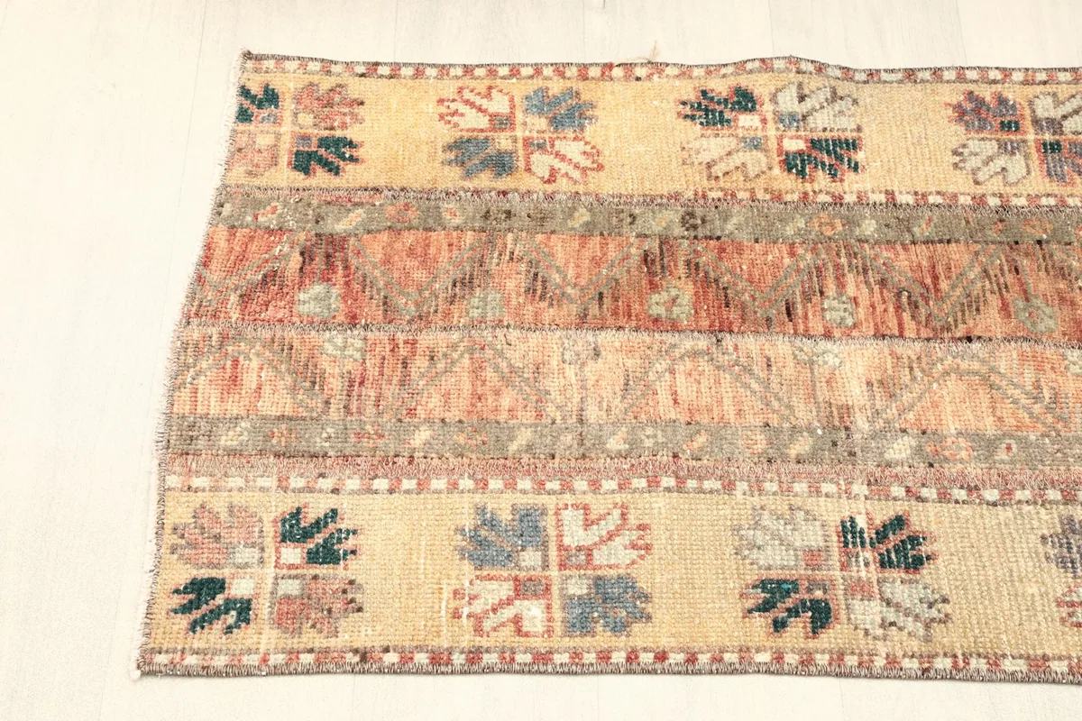 View of one side of the rug, showcasing the beige border with blue, green, and purple tribal motifs.